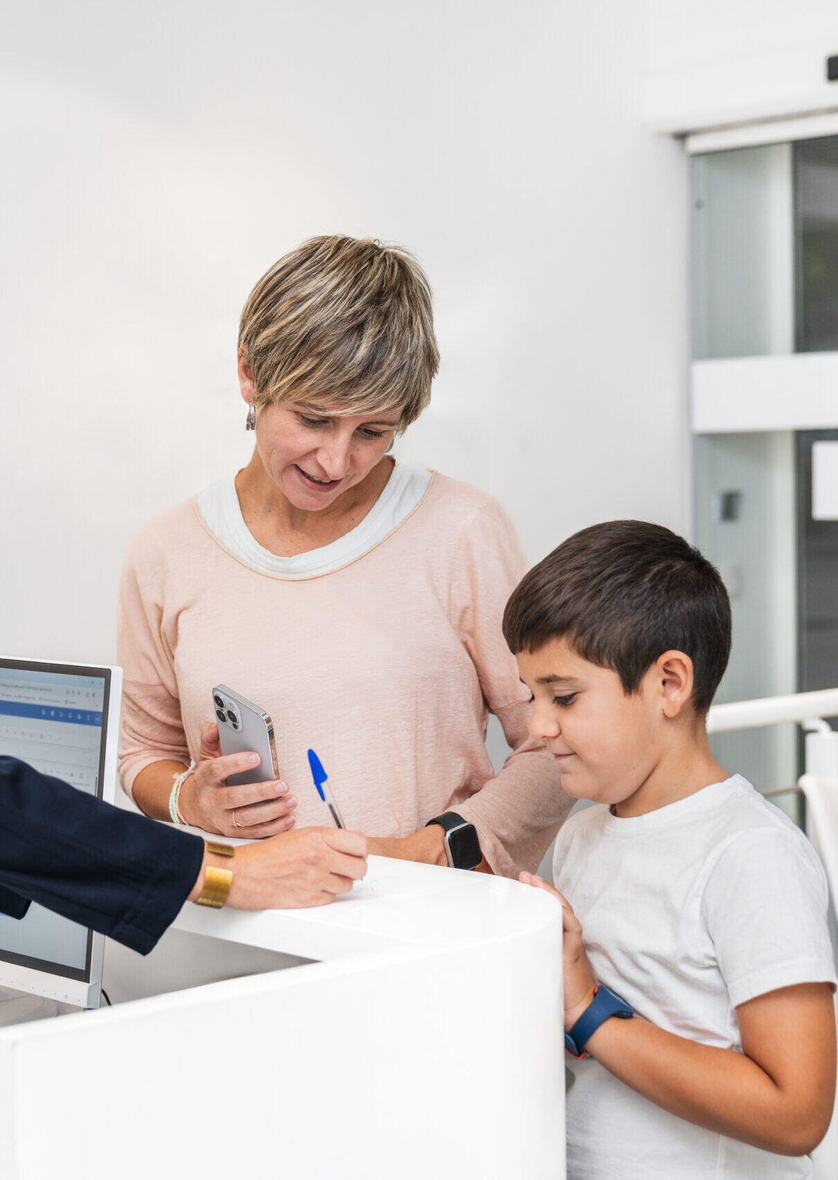 Boy smiling with mother at the dentist's reception desk, registering for dental checkup.