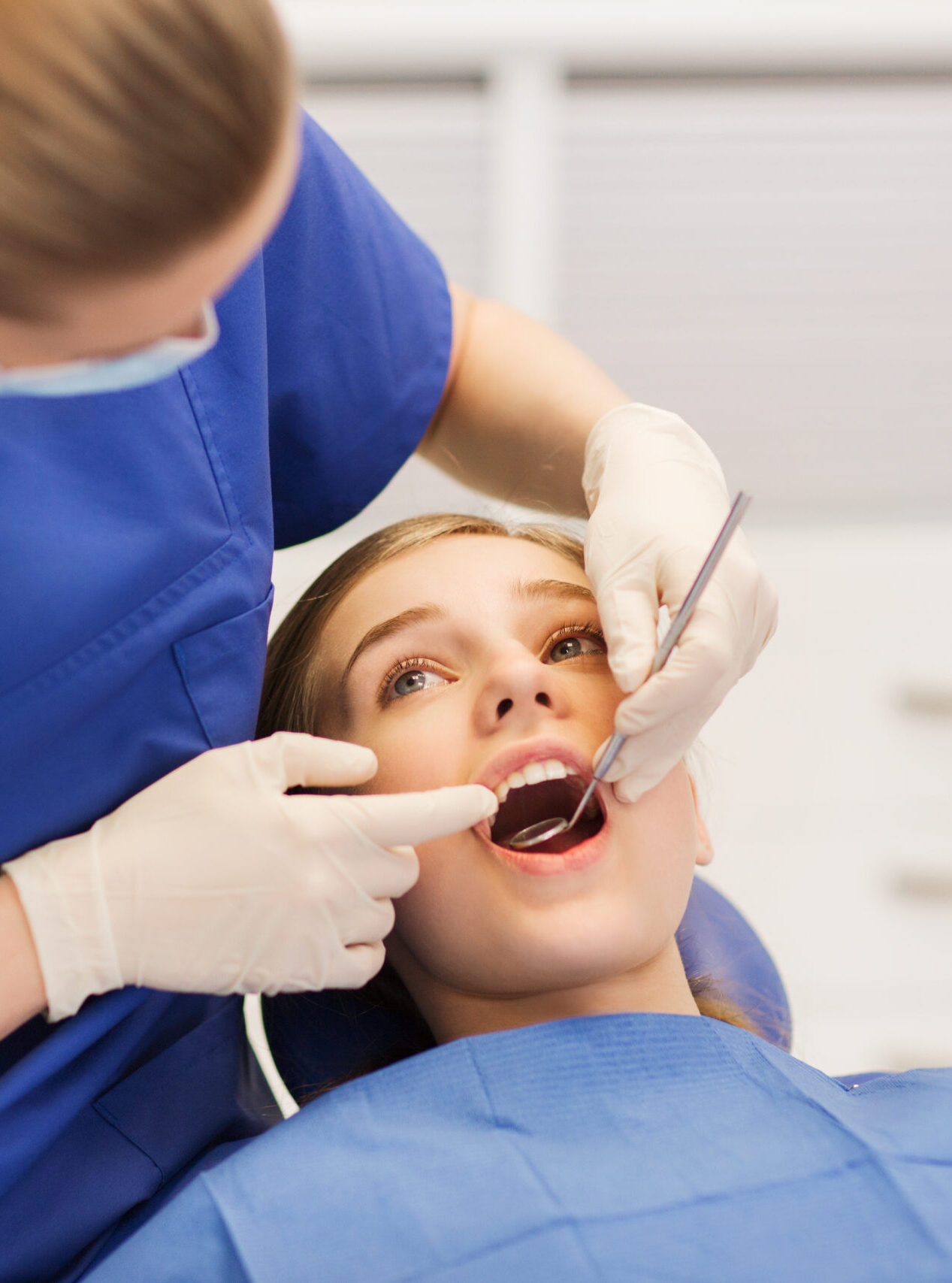 people, medicine, stomatology and health care concept - happy female dentist with mirror checking patient girl teeth up at dental clinic office