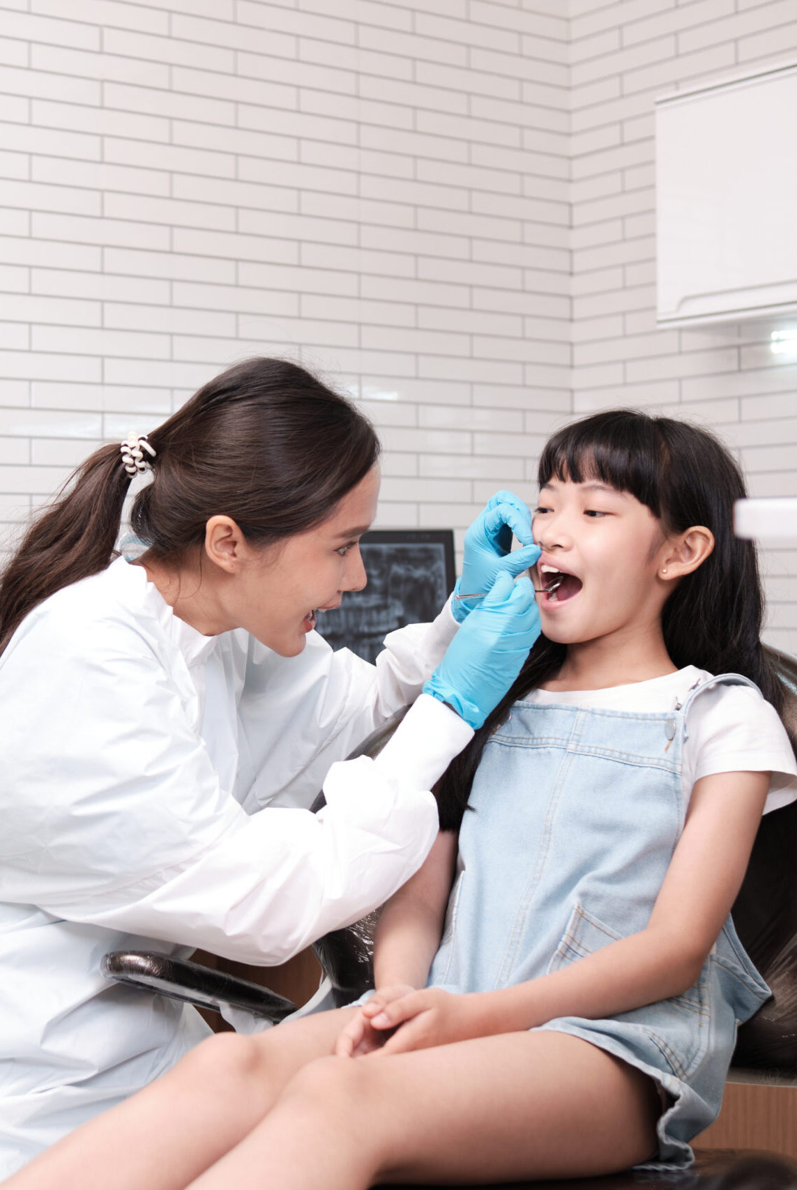 Asian female pediatric dentist and assistant check and examination a little girl's caries teeth in dental clinic, well-being hygiene, and professional orthodontic healthcare work in kid hospital.