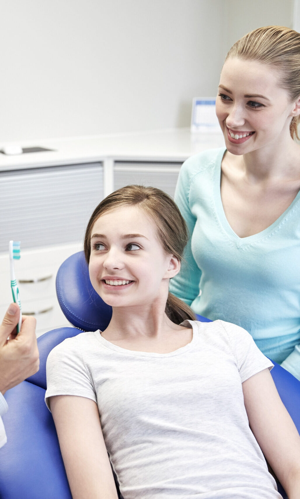 people, medicine, stomatology and health care concept - happy male dentist showing toothbrush to patient girl and her mother at dental clinic office