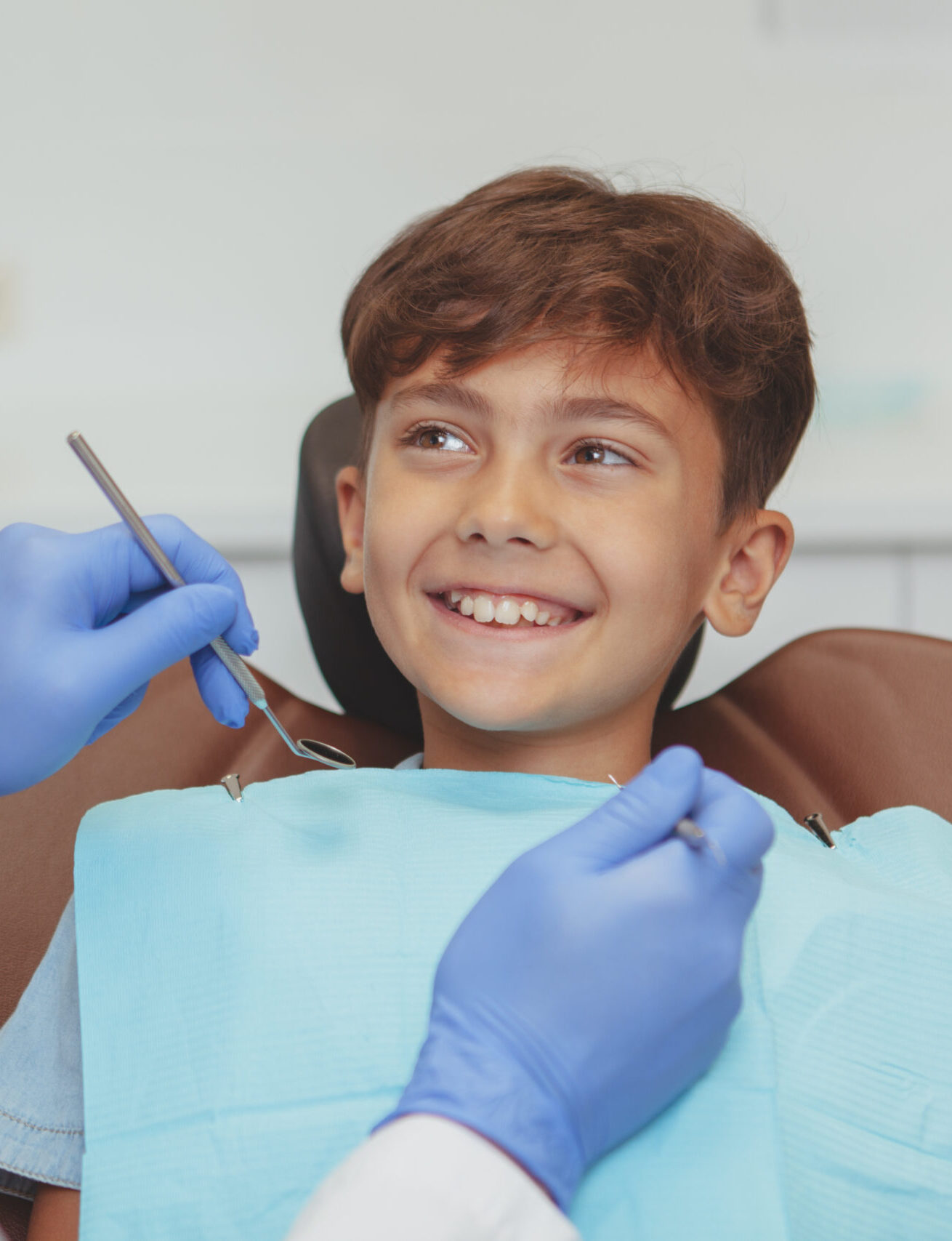 Adorable happy healthy boy smiling cheerfully at his dentist, sitting in a dental chair. Cropped shot of a professional dentist checking teeth of a lovely boy