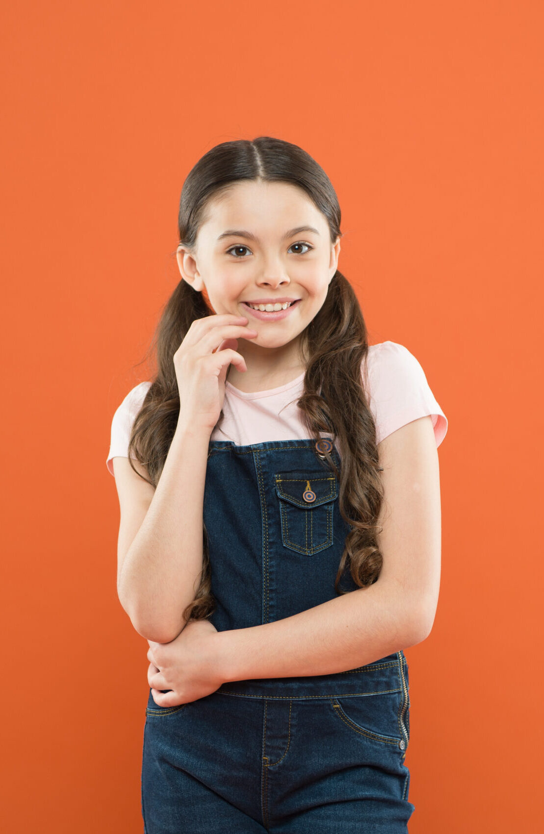 Nothing beats a great smile. Adorable little girl with big smile on orange background. Smiling child with white healthy smile on beautiful face. Cute small kid with long brunette hair and happy smile.