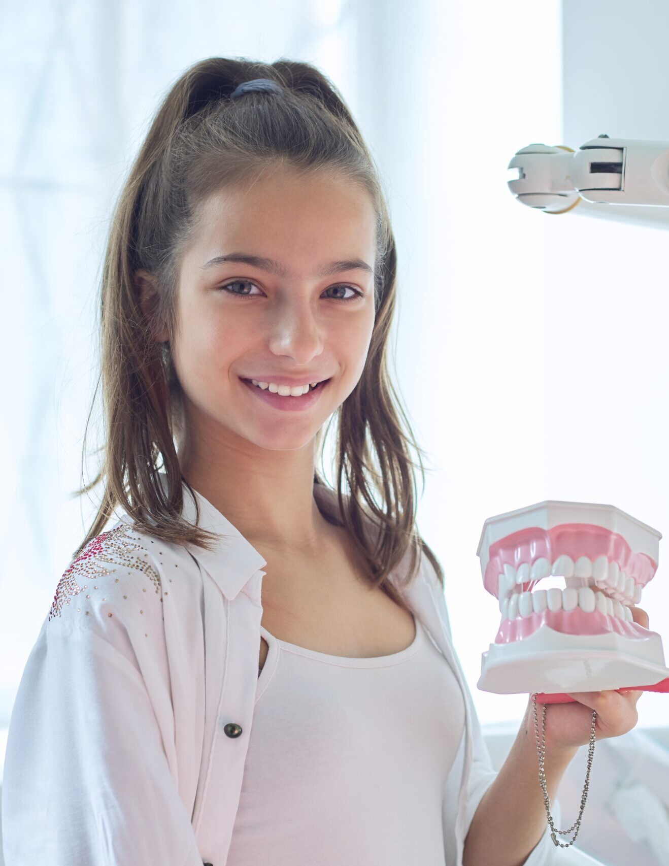 Smiling teenager girl in dental office holding jaw model with teeth in her hands
