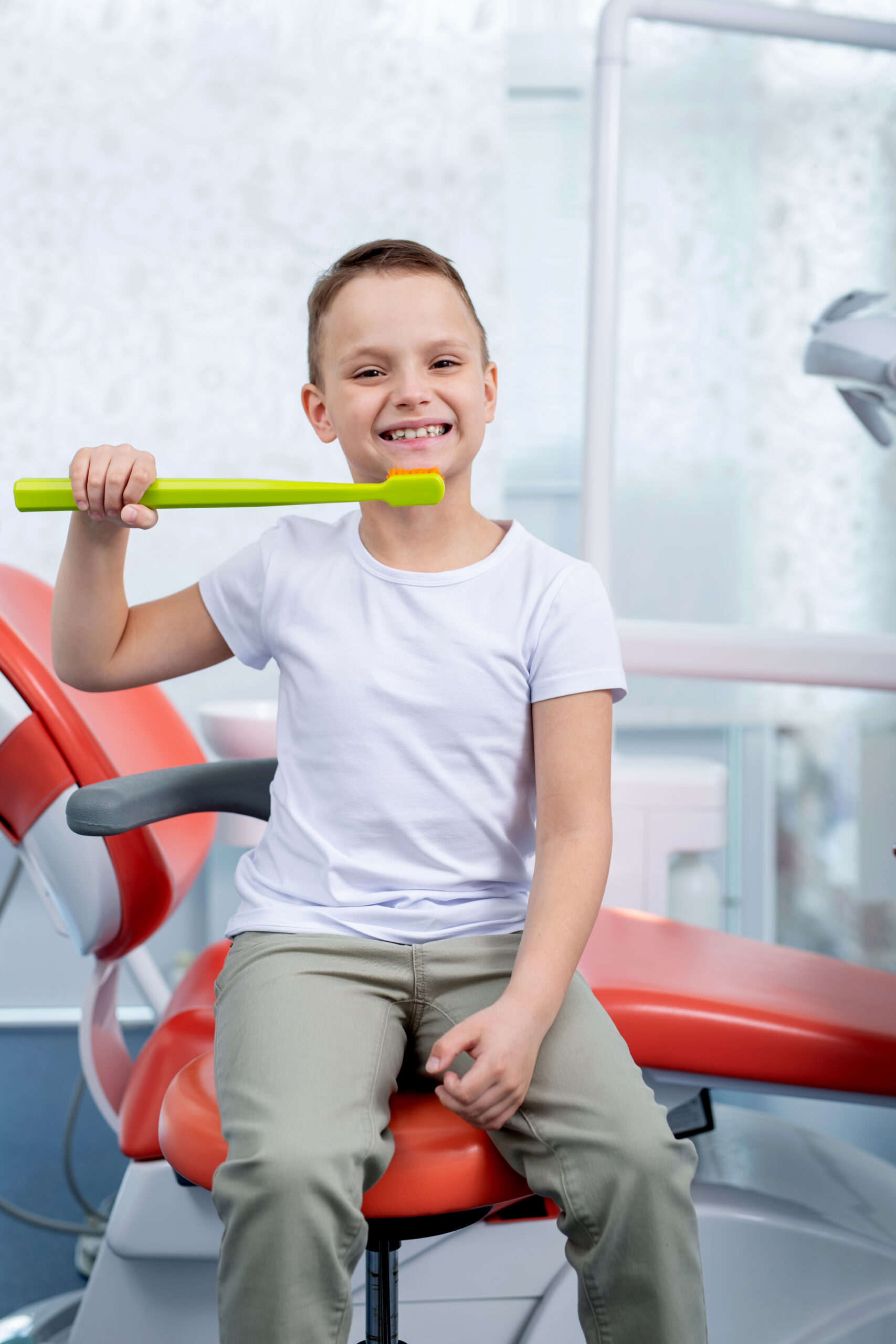 little boy child laughs at a dentist appointment. boy shows how to brush his teeth with big green toothbrush. Concept - checking caries in children