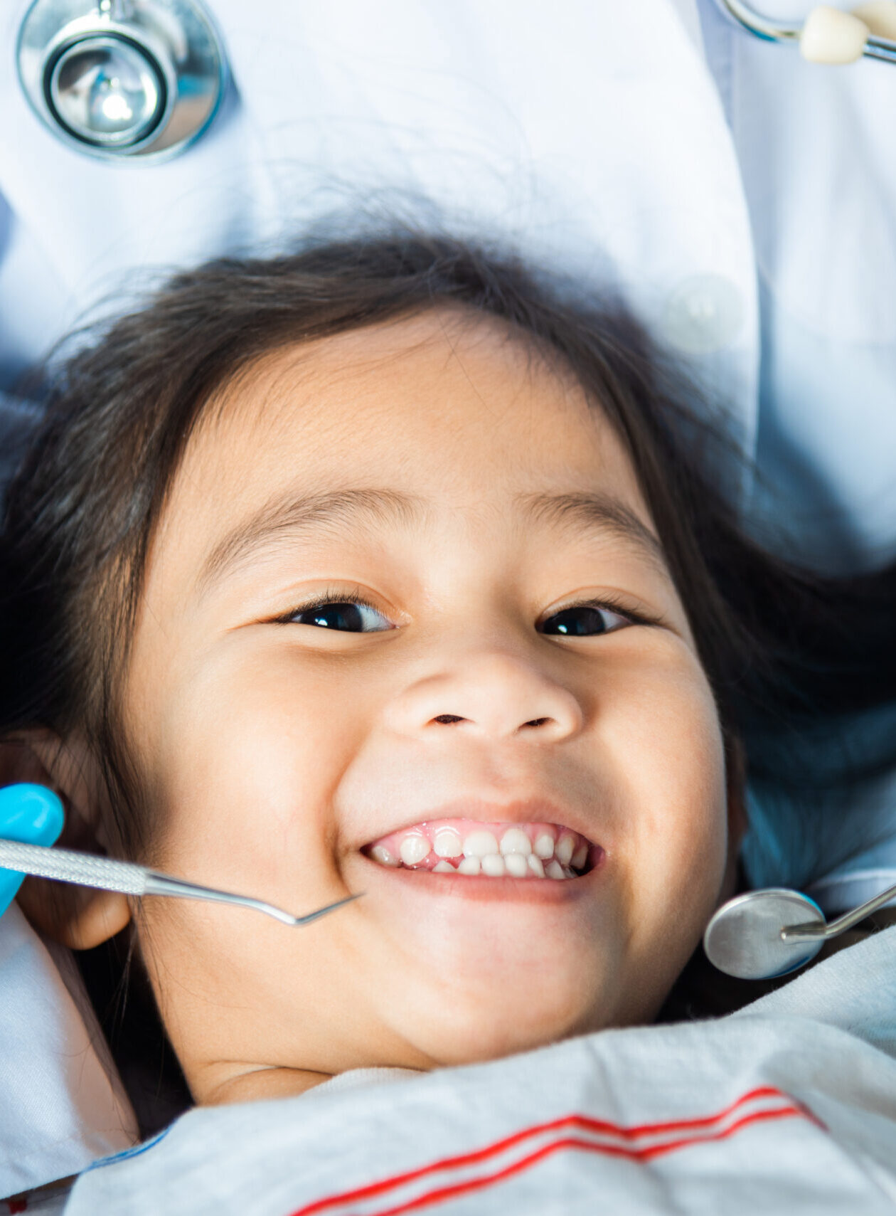 Dental kid health examination. Doctor examines oral cavity of little child uses mouth mirror to checking teeth cavity, Asian dentist making examination procedure for smiling cute little girl