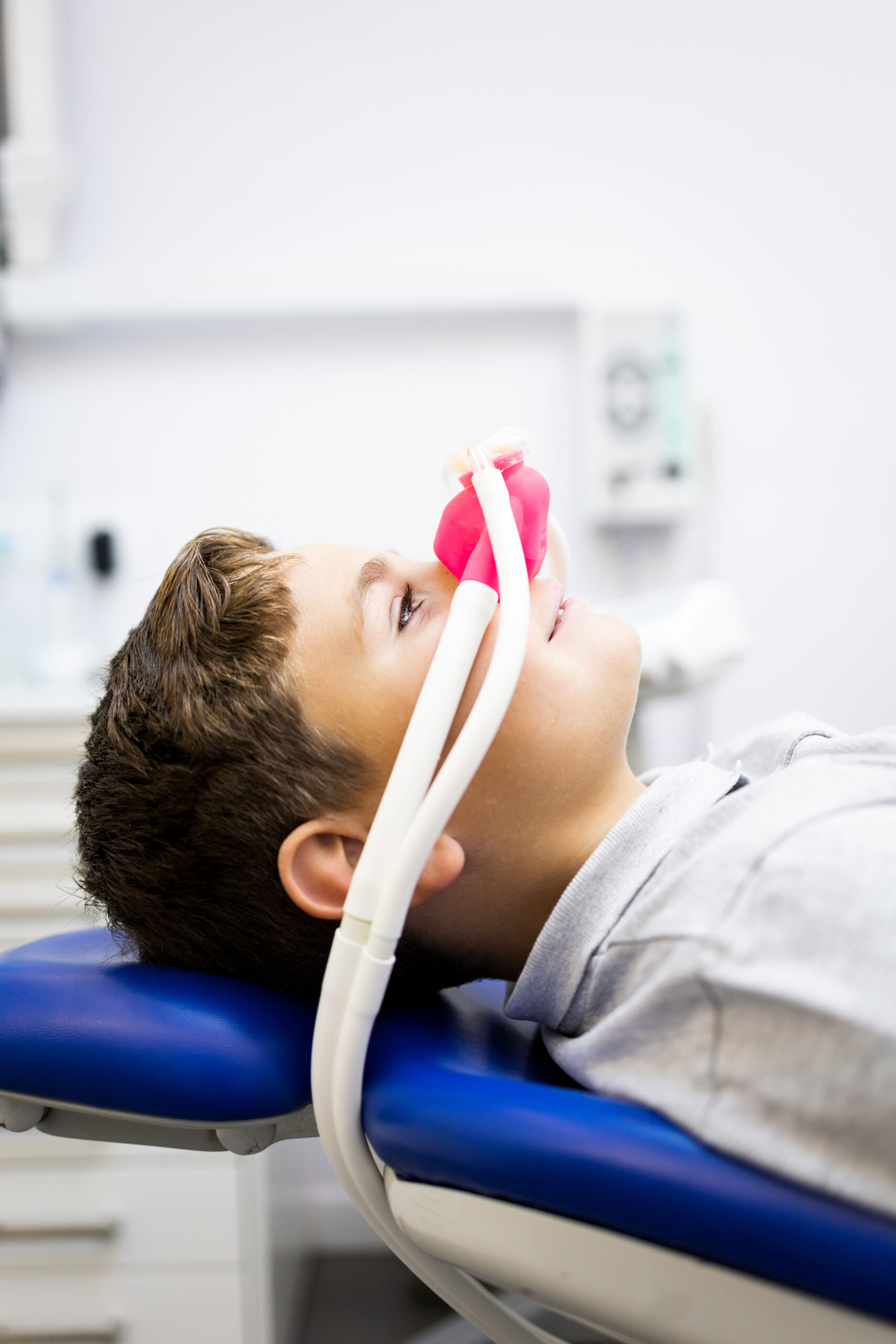 Fear of the dentist! Vertical photo of a little boy sits in a dentist's office wearing a nasal mask breathing nitrous oxide to relax. Concept of feeling relaxed with laughing gas.