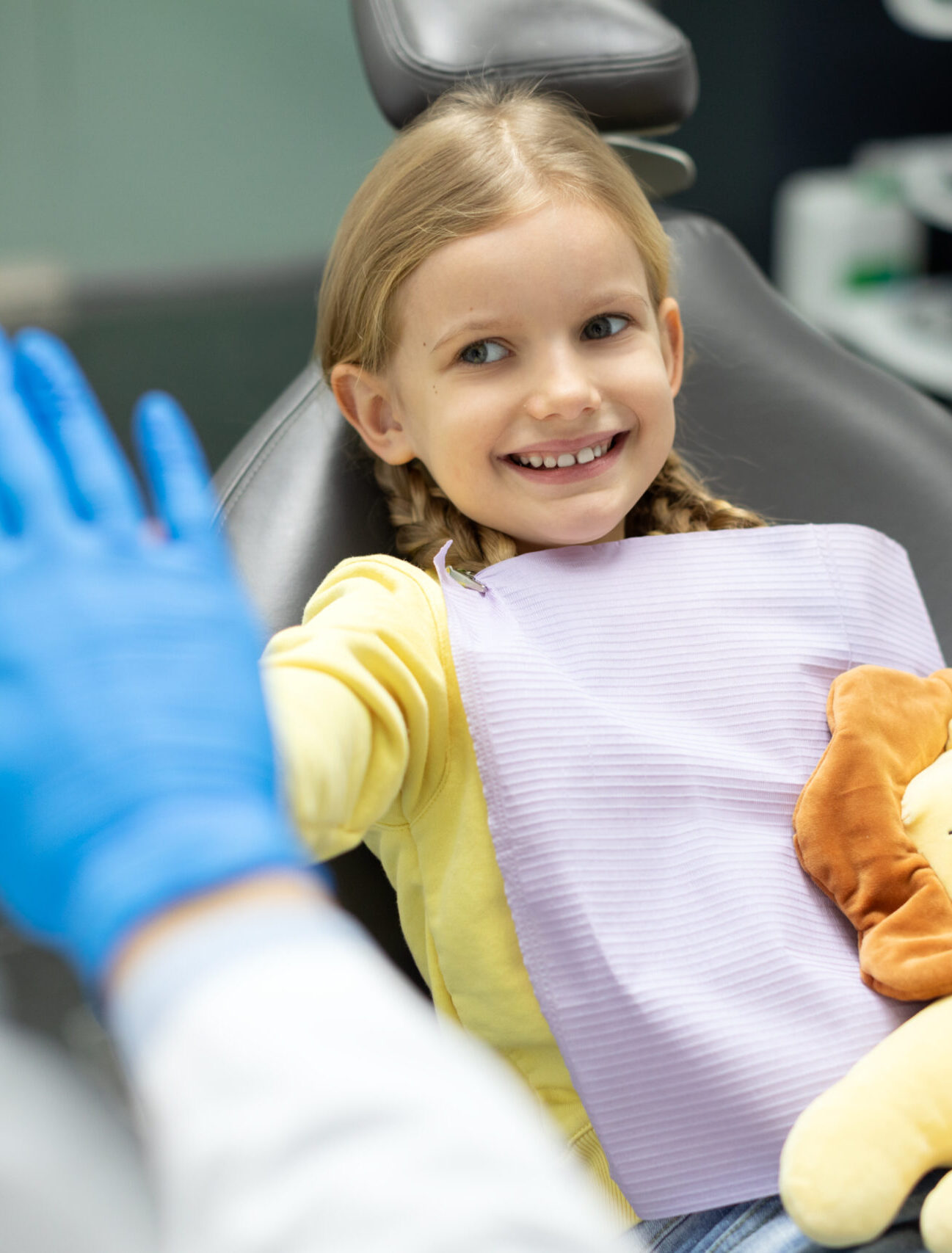 Children's dentistry. Smiling child girl sitting in the dental chair and cheerfully gives high five to male doctor
