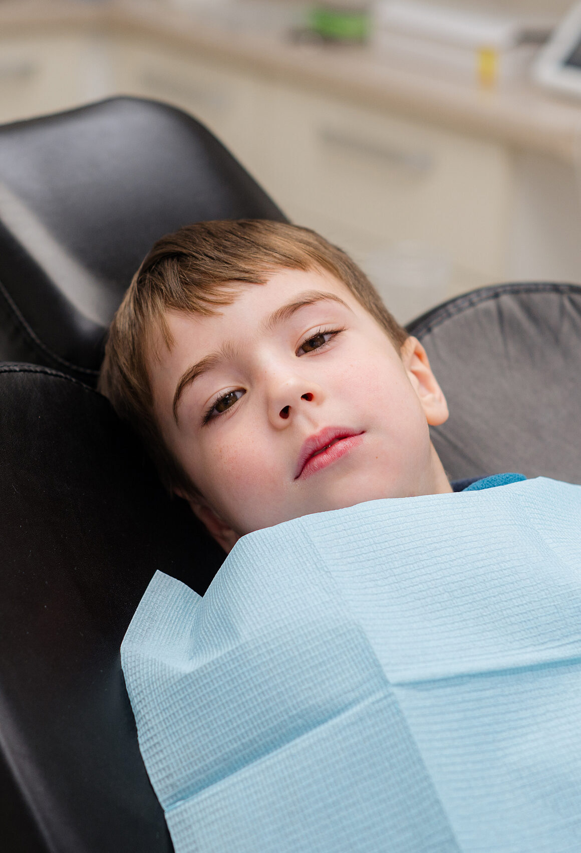 A cute little boy in a dental chair treats his teeth, smiling and happy
