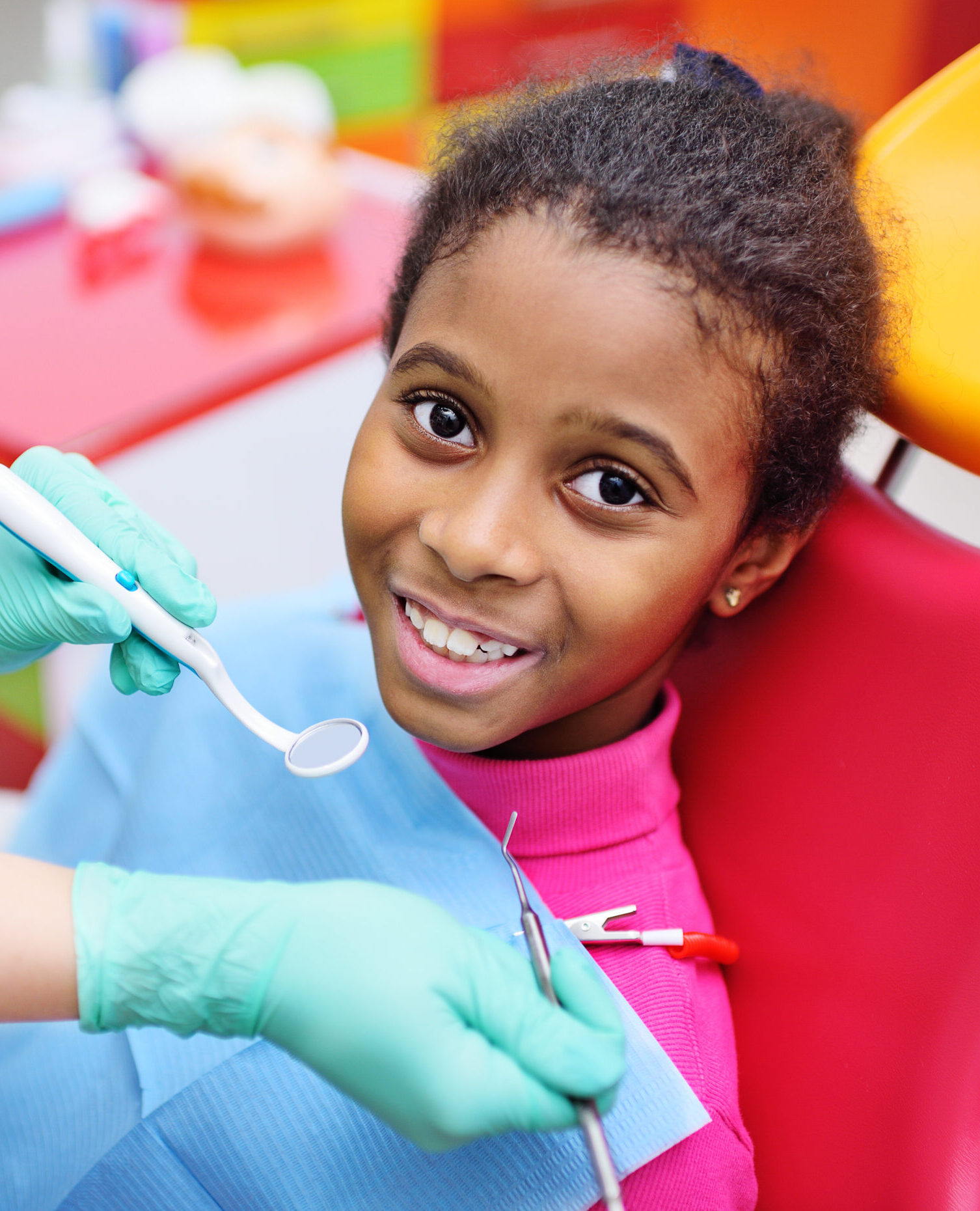 African American baby girl smiling sitting in a dental chair at the examination of the pediatric dentist.