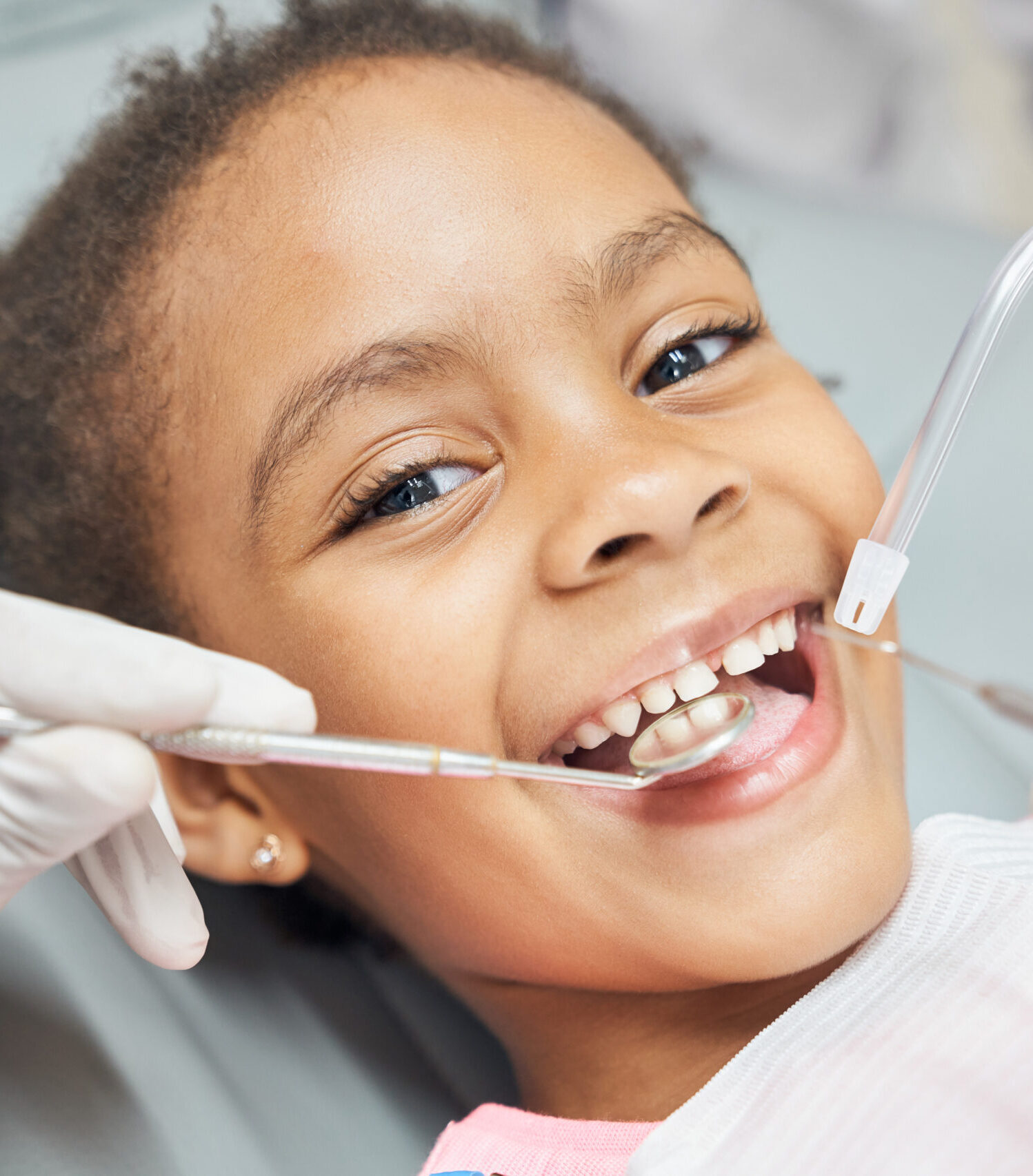 Charming little afro american girl sitting in dental chair, smiling and looking at camera during medical treatment at modern clinic. Concept of health care ad pediatrics