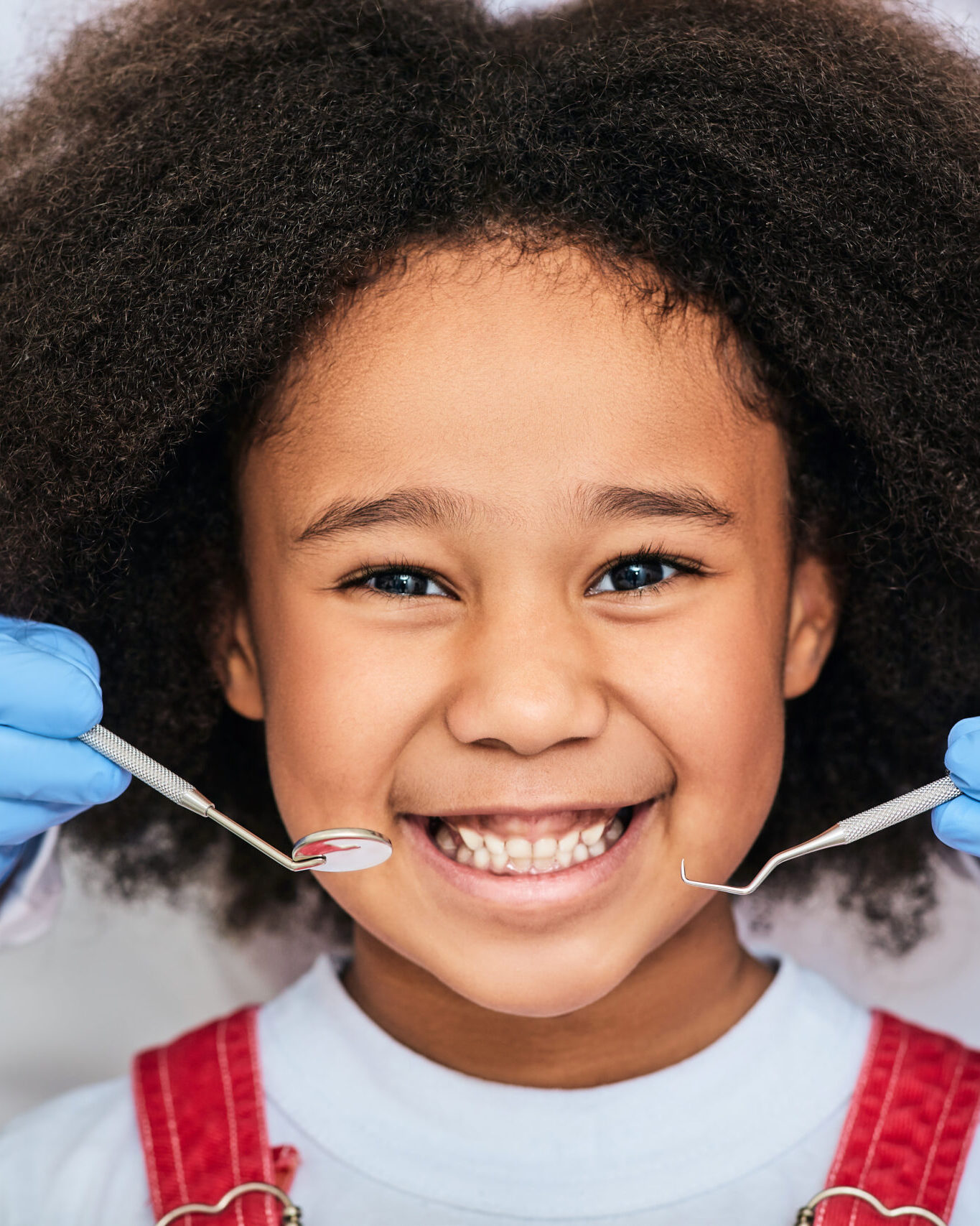 African American little girl with a toothy smile during an inspection of oral cavity by a dentist. Child in a dental clinic for children, cropped