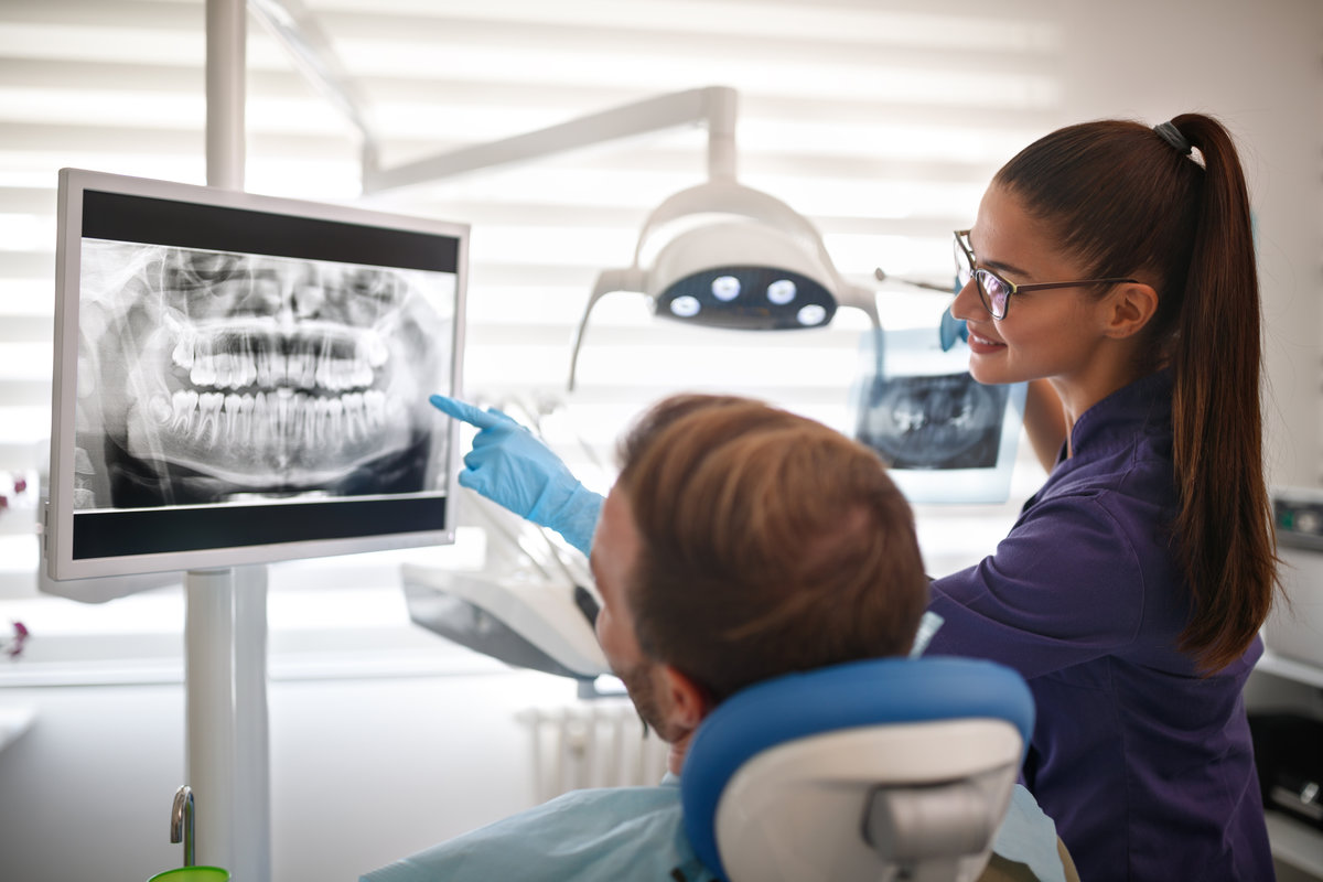 Female dentist showing x-ray footage of teeth to male patient in clinic